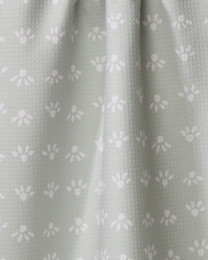 The "Sun Bursts" tea towel by Anee Shah features light gray fabric with a subtle texture, small white paw prints, and gentle vertical folds. Ultra-absorbent and charming, it's perfect for your kitchen.
