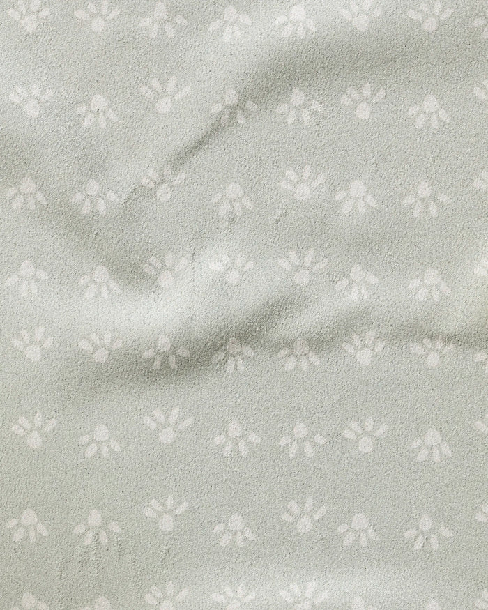 The Sun Bursts towel by Anee Shah is ultra-absorbent, light grey, and features a subtle small white paw print pattern with a slightly wrinkled, textured surface.