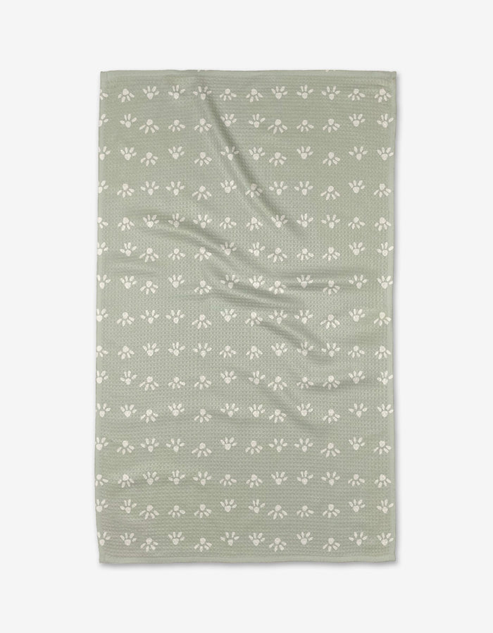 The Anee Shah Sun Bursts tea towel is green, rectangular, made from recycled materials, and features a textured surface with rows of small white paw prints across the fabric.