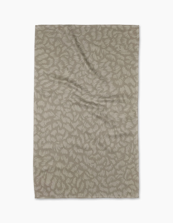 A rectangular, beige Sun Kissed tea towel by Geometry, crafted from eco-friendly Geoweave fabric with an abstract leaf pattern, is laid flat on a white background.