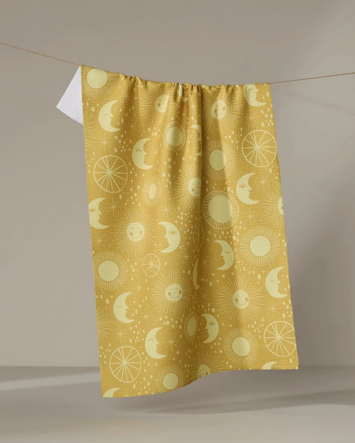 The Sun Moon Star kitchen tea towel by Jessica Swift features pale celestial patterns on yellow, made from recycled materials and displayed against a neutral background.