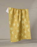 The Sun Moon Star kitchen tea towel by Jessica Swift features pale celestial patterns on yellow, made from recycled materials and displayed against a neutral background.