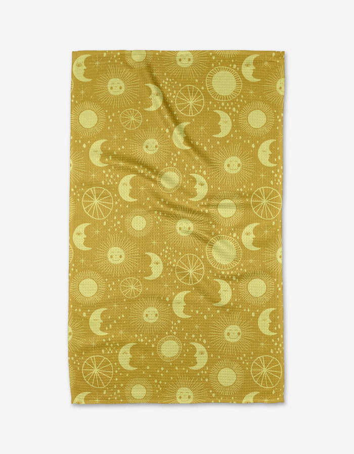 Jessica Swift’s Sun Moon Star blanket in mustard yellow features repeating suns, moons, stars, and geometric circles in lighter yellow. Shown laid flat with gentle wrinkles. Eco-friendly design.