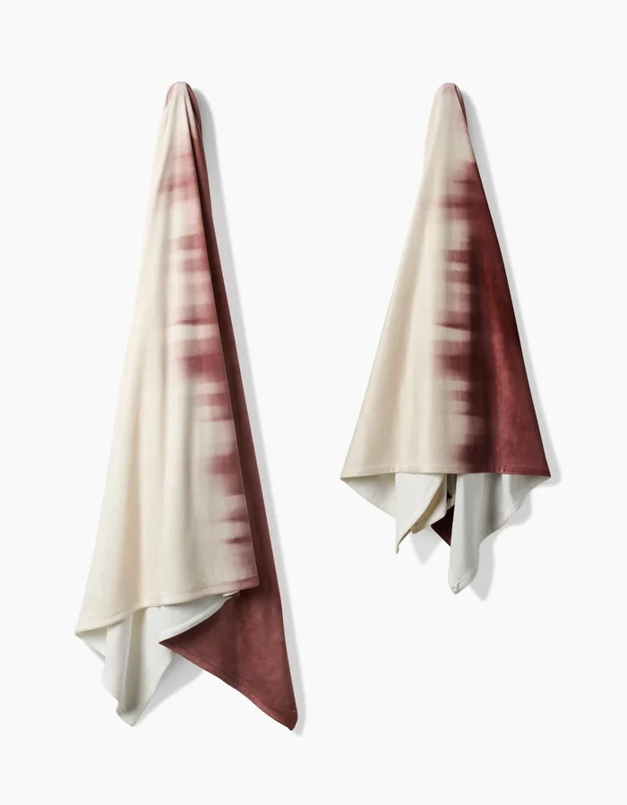 Two Sundae towels by Geometry hang side by side on hooks, each featuring a white and deep maroon tie-dye pattern. Their soft gradient design evokes the cozy comfort of a Butter Blanket, blending style and luxury on both sides.