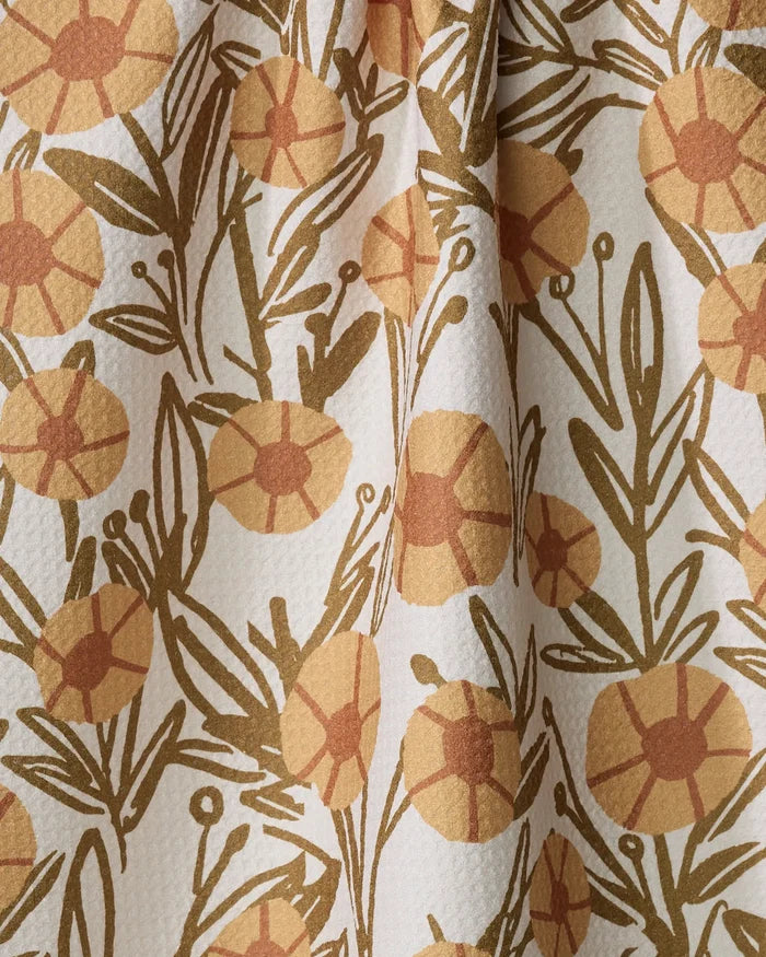 A close-up of the "Sunflower Fields" tea towel by Janna Sue Design shows yellow and orange floral patterns with greenish-brown leaves on a textured white background. This ultra-absorbent towel is softly folded.
