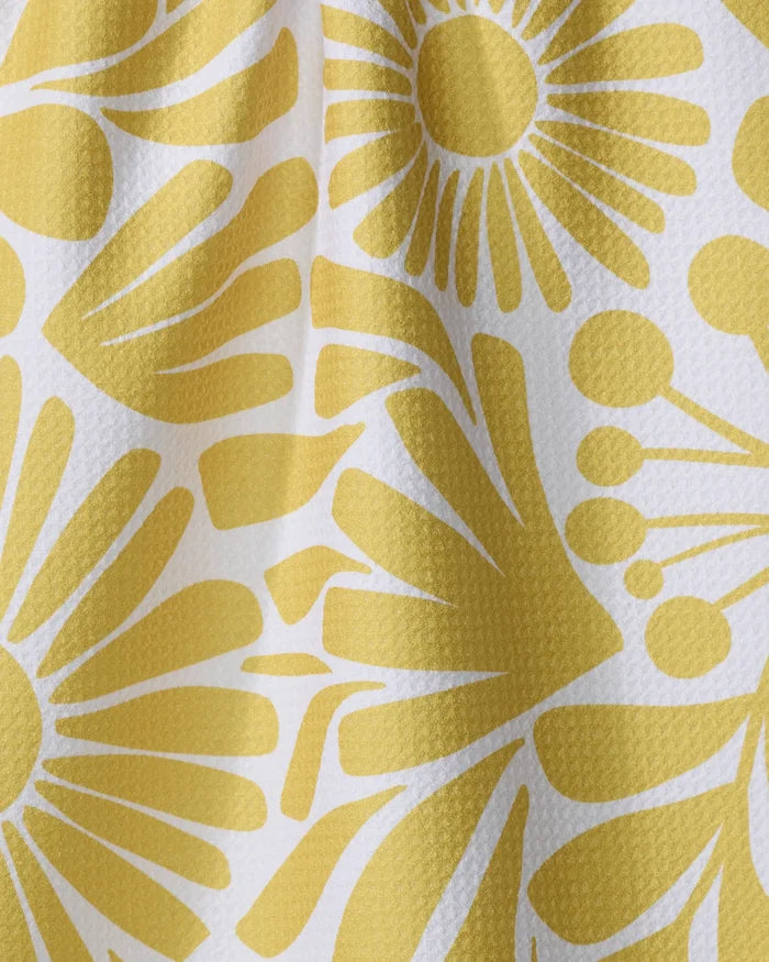 Close-up of Lisa Nelson's Sunlit Blooms kitchen towel, made from textured white recycled material and adorned with a yellow abstract floral pattern featuring stylized flowers and radiating petals, with gentle folds and shadows visible.