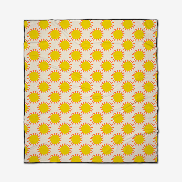 The Sunny Day rectangular beach blanket by Lizzie Clark features yellow suns with orange rays on a white background. Made from quick-drying recycled materials, it has a slightly wrinkled appearance.
