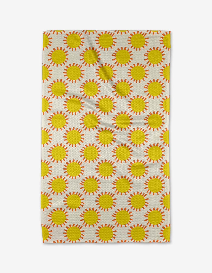 The Sunny Day Tea Towel by Lizzie Clark features a repeating pattern of yellow suns with orange rays on a light background. Made from Geoweave™ fabric, it has visible creases and is displayed on a white surface.