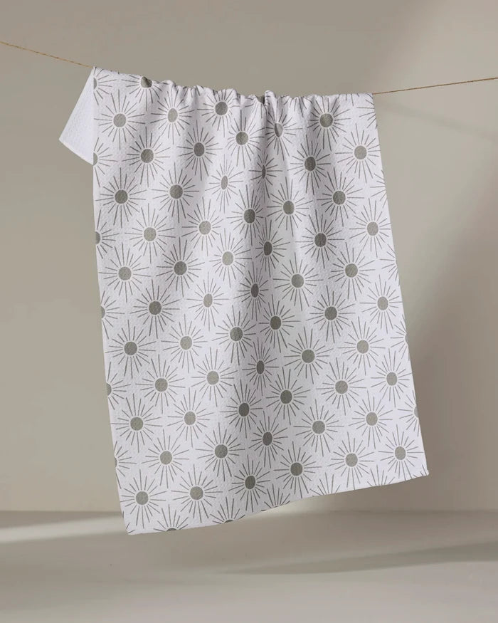 The Hufton Studio Sunny Geo towel, featuring a white ultra-absorbent fabric with a repeating gray geometric sunburst pattern, hangs on a clothesline against a neutral background.