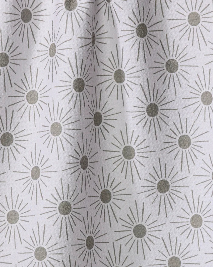 The Hufton Studio "Sunny Geo" tea towel features a white fabric with repeating gray sunburst patterns, each with a solid circle center and radiating lines, draping softly to create gentle folds and shadows.