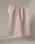 The Rosa Kichline "Sunrise Mosaic" recycled tea towel in blush pink and white features a geometric fan pattern and hangs from a string against a neutral beige background.