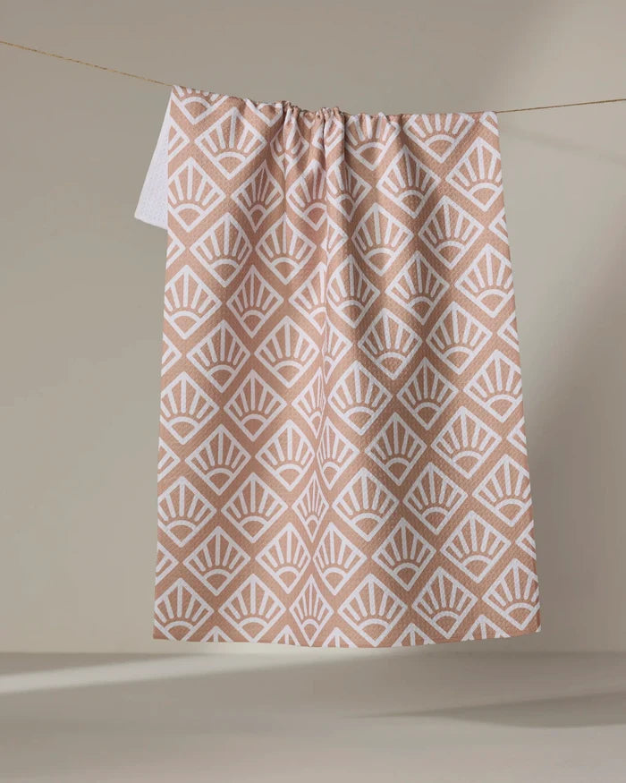 The Rosa Kichline "Sunrise Mosaic" recycled tea towel in blush pink and white features a geometric fan pattern and hangs from a string against a neutral beige background.