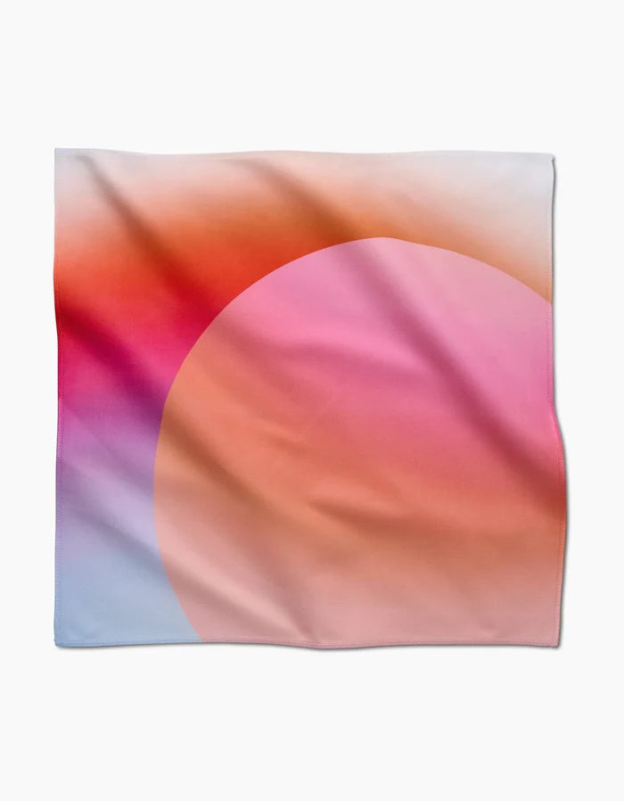 Sunrise by GEOMETRY is a square scarf made from recycled materials, featuring a soft gradient with a large pink and orange circle on a blue, purple, red, and white background. The smooth fabric drapes in gentle folds.