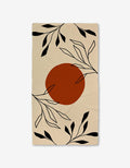 The GEOMETRY Sunset Bath is a beige rectangular Luxe Bath Towel featuring a large burnt orange circle in the center and black abstract leaf and branch designs, crafted with ultra-absorbent Geoweave technology.