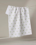 The Danelys Sidron "Sunshine Glow" tea towel, white with a textured surface and light green polka dots, hangs on a clothesline against a neutral background.