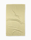 The GEOMETRY Sunspread tea towel features a yellow and white checkered pattern with subtle wrinkles, laid flat on a white background, and is crafted from recycled materials.