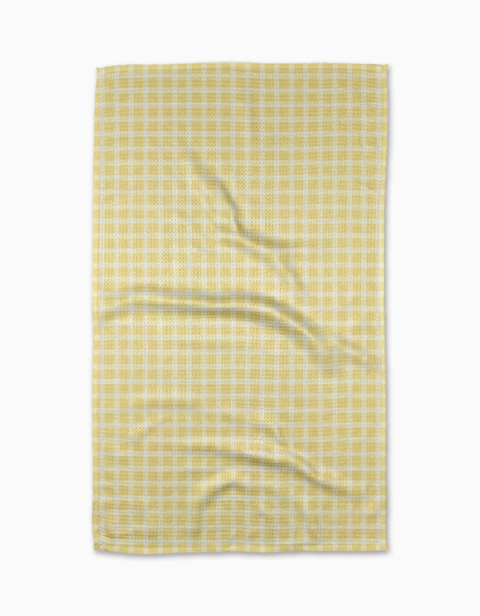 The GEOMETRY Sunspread tea towel features a yellow and white checkered pattern with subtle wrinkles, laid flat on a white background, and is crafted from recycled materials.
