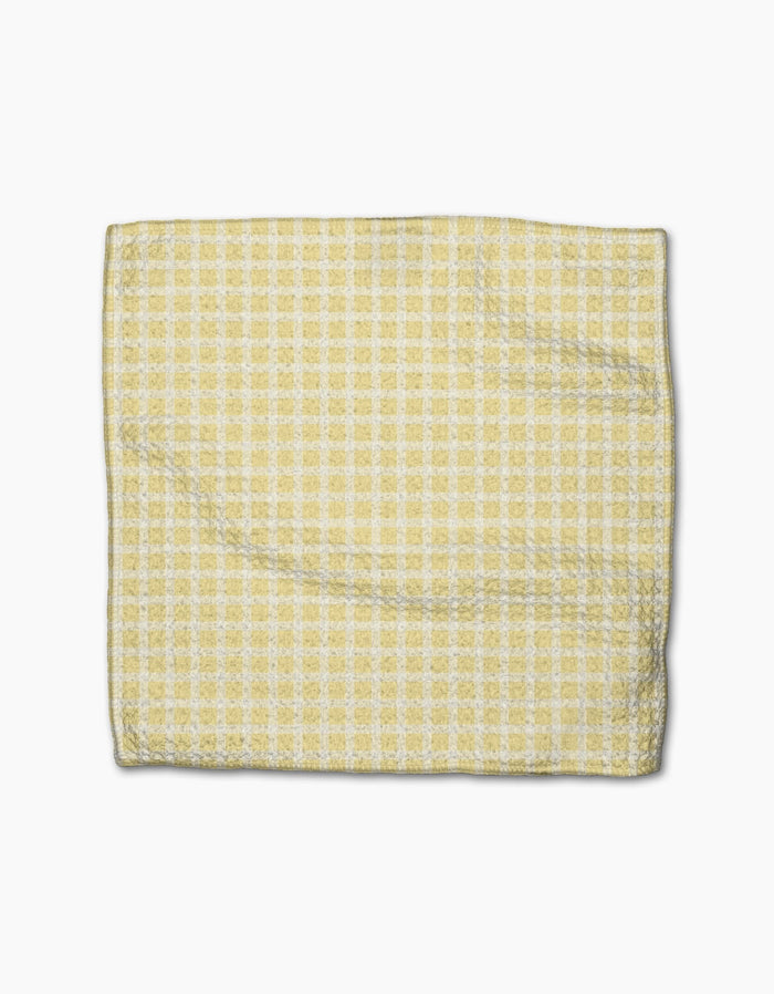 The GEOMETRY Sunspread napkin, featuring a yellow and white checkered design and made from recycled materials, is shown folded on a plain white background.