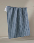 The Buy Guide’s Super Stripe - Navy kitchen towel, made from recycled materials, hangs from a thin line with blue and gray vertical stripes and a subtle texture—perfect as an absorbent dish towel against a neutral beige background.