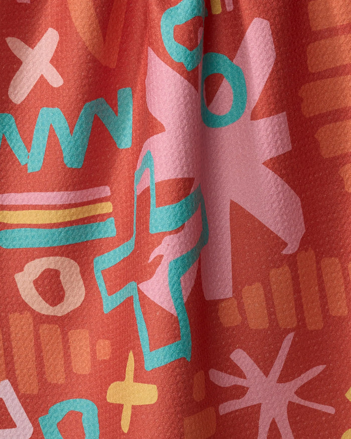 A close-up of the Sareka Unique Superstar quick-drying towel, featuring a vibrant abstract pattern with pink, teal, yellow, and orange geometric shapes on a red background. The fabric is slightly gathered or draped.