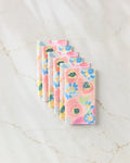 Six eco-friendly Suzzy and Margot paper towels by Ania Zwara Art are neatly stacked on a white marble surface. The napkins display pastel pink, blue, and yellow flowers with green leaves.
