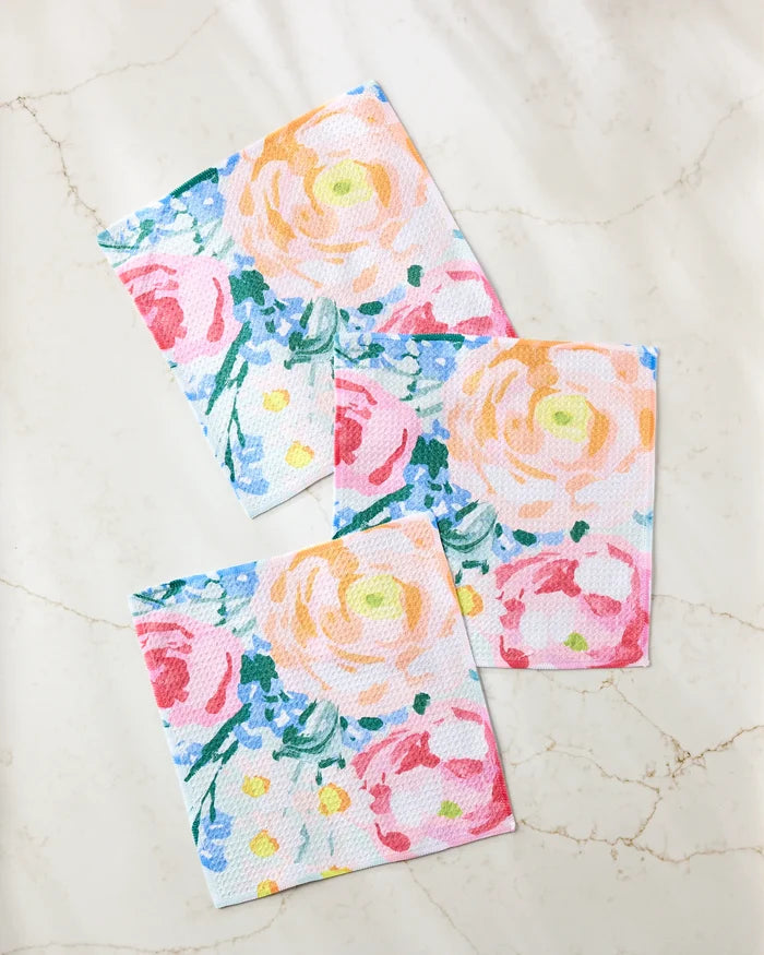 The Suzzy dishcloth set by Ania Zwara Art includes three super-absorbent towels featuring a vibrant floral pattern with pink, peach, and yellow flowers plus green leaves on a light marble background.