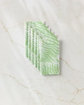 Six Swaying Leaf napkins by GEOMETRY, featuring a green leaf pattern inspired by eco-friendly kitchen towels, are arranged neatly on a white marble surface with beige veining.