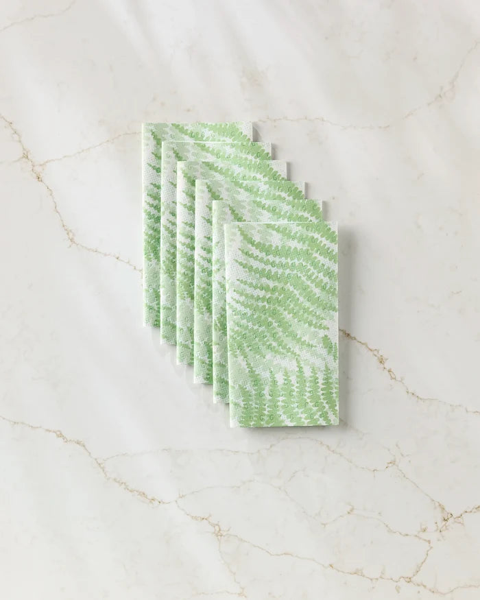 Six Swaying Leaf napkins by GEOMETRY, featuring a green leaf pattern inspired by eco-friendly kitchen towels, are arranged neatly on a white marble surface with beige veining.