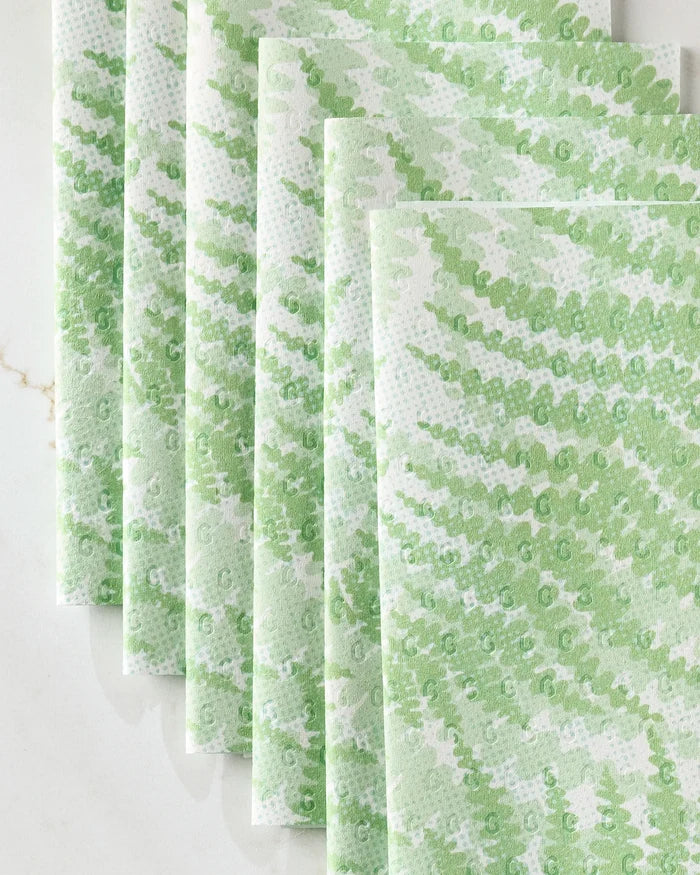 Six eco-friendly Swaying Leaf kitchen towels by GEOMETRY, featuring a white base with a green leaf pattern, are neatly overlapped on a light surface.