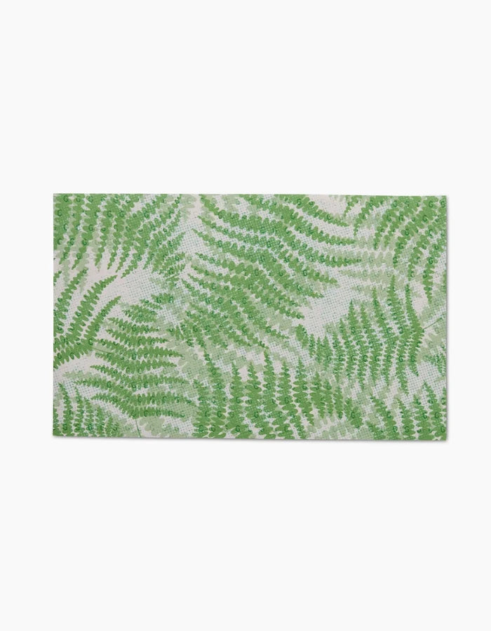 The GEOMETRY Swaying Leaf mat features a green fern leaf pattern on a light beige background and is made from eco-friendly, post-consumer recycled materials.
