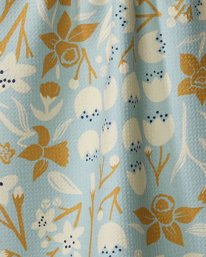 The "Swedish Cherry Blossoms" tea towel by Elisabeth Wing features a light blue background with mustard yellow, white, and black floral patterns. Made from recycled materials, it has a slightly textured finish.