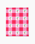 The Geometry Sweet Cherry Gingham throw blanket features a pink and red checkered pattern with white squares, each adorned with two red cherries and green leaves—adding cozy, cheerful comfort to any space.