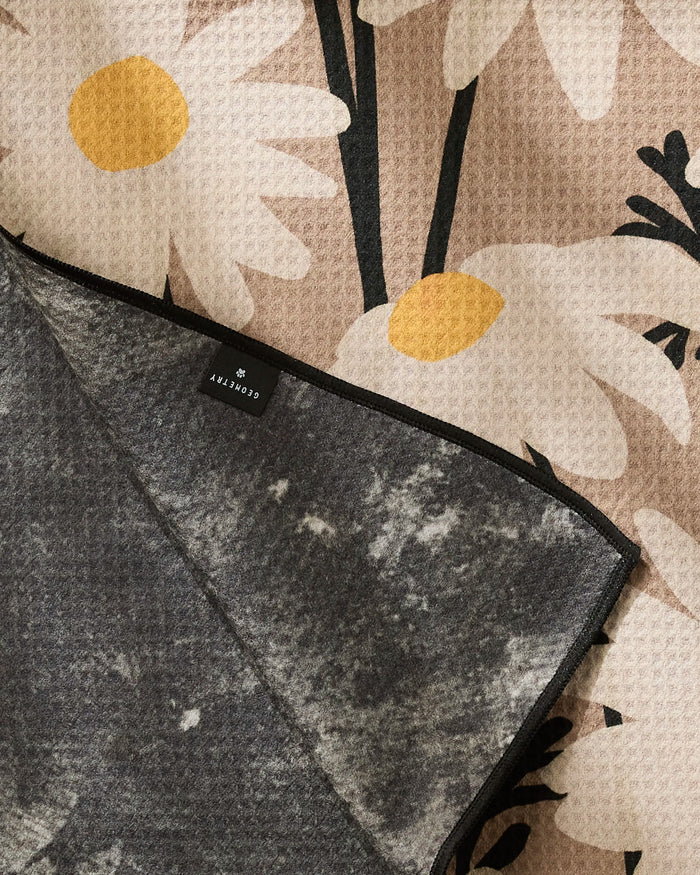 The Geometry Sweet Daisies dog towel features a beige and white daisy floral pattern on one side, a gray marbled design on the other, and a visible “Crosby” tag, shown partially folded to display both looks.
