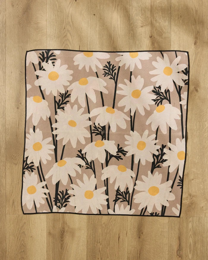 The "Sweet Daisies" rug by Geometry, made from recycled materials, has large white daisies with yellow centers and black stems and leaves, shown on a light wood floor.