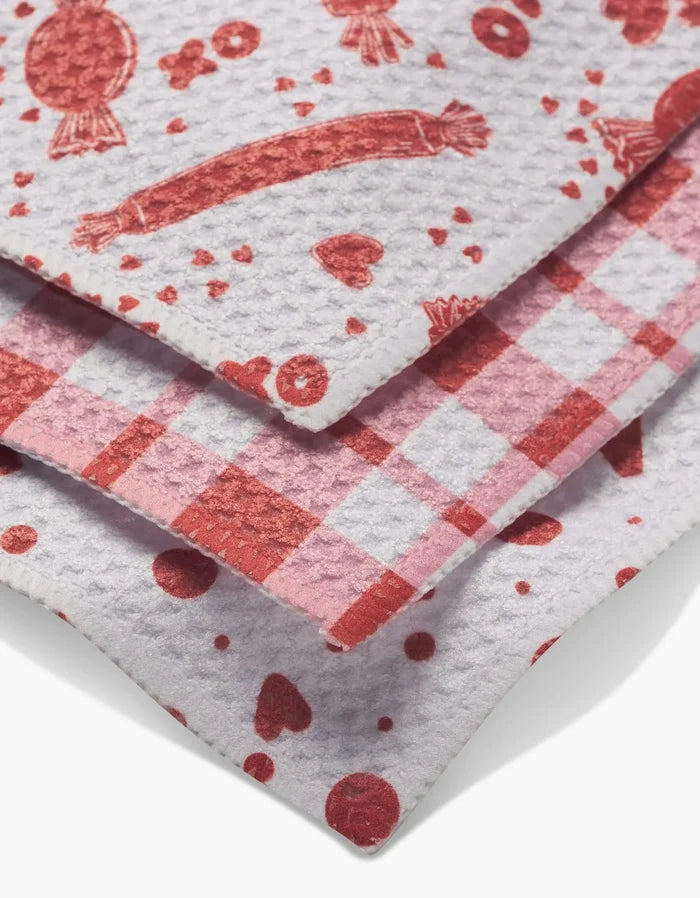 The Sweet Love dishcloth set by Charlie Rowan Designs includes three white textured Geoweave cloths, each stacked with a unique red pattern: candies and hearts, a checkered print, and scattered dots with hearts.