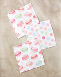 Three Elena Fay "Sweet Macarons" recycled napkins are shown on a beige surface—two with pastel macarons, one with pink, green, blue, and orange polka dots.