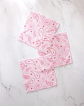 Three 'Sweet Paisley' napkins by GEOMETRY, featuring a pink paisley pattern and made from recycled materials, are displayed on a white marble surface.