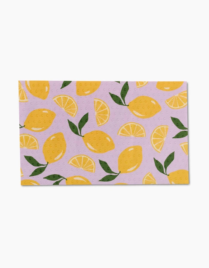 The GEOMETRY Sweet Summer Mix 1 is a rectangular, eco-friendly dishcloth featuring whole lemons, lemon slices, and green leaves on a light purple background—a charming alternative to Not Paper Towels.