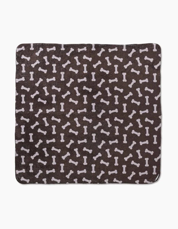 Geometry’s “Sweet Treats” is a square, dark brown plush dog towel with a white dog bone pattern, made from ultra-absorbent recycled materials.