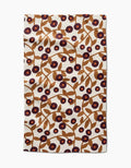 The Lizzie Clark Swirling Vines tea towel is rectangular, made from recycled materials, and features brown branches with leaves and purple and red circular flowers on a cream background.