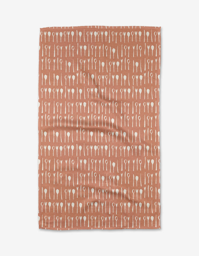 The Tableware tea towel by Anee Shah features a rust hue and is made from Geoweave fabric, with a white utensil pattern—forks, knives, and spoons—displayed in neat horizontal rows.