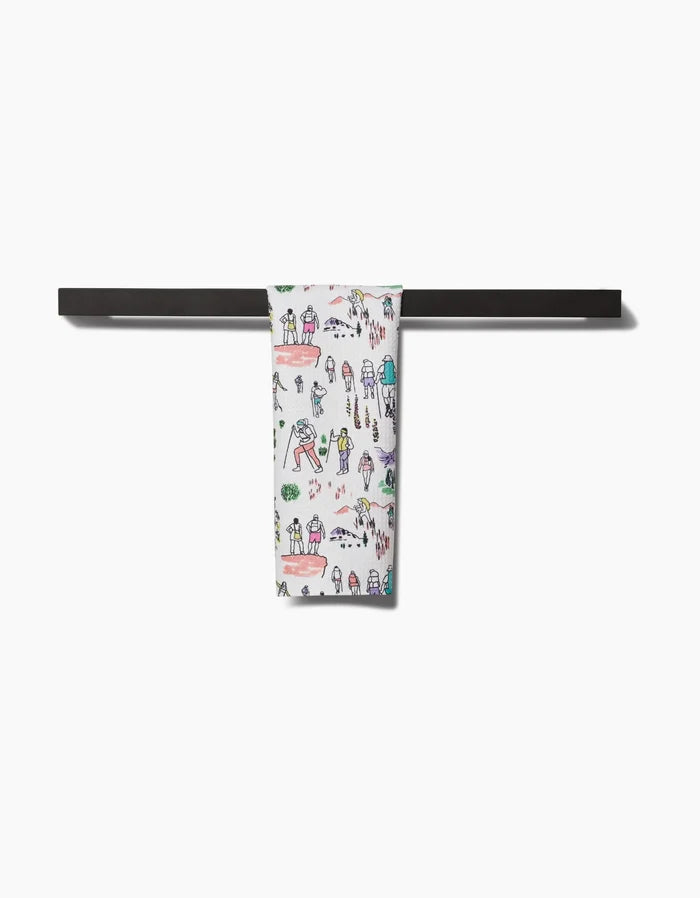 The Take A Hike Bar Towel by Elisabeth Wing, featuring playful hand-drawn people and trees on ultra-absorbent Geoweave fabric, hangs neatly on a black towel bar, standing out against the white background.
