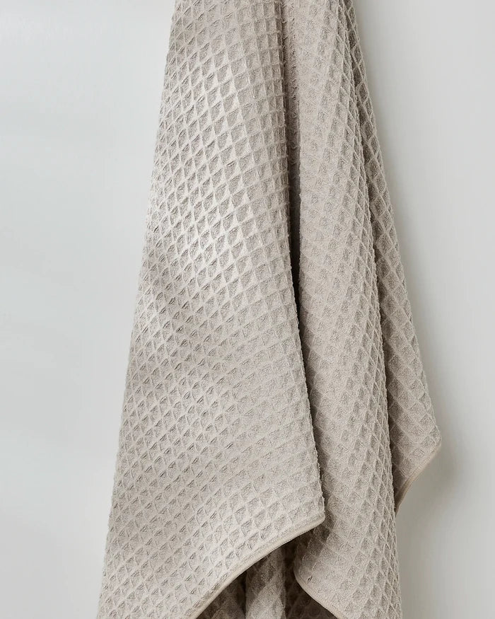 The GEOMETRY Taupe waffle bath towel with a textured finish hangs folded on a white wall, bringing luxurious style to your bathroom.