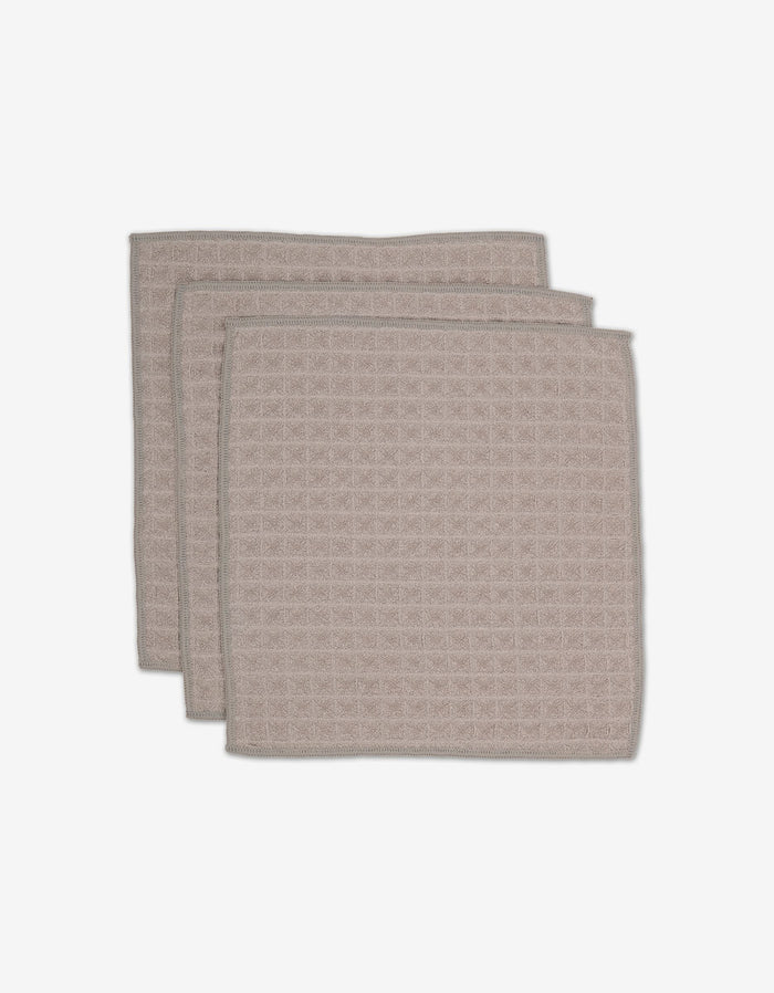 Three taupe GEOMETRY Waffle Washcloths, made from recycled materials, are stacked slightly offset against a white background.