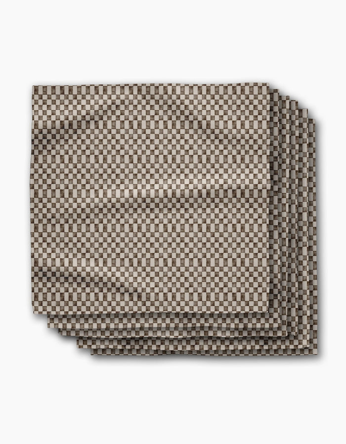 A set of four eco-friendly “Tavern” napkins by Geometry, neatly folded and displaying a small brown and white checkerboard pattern against a white background.