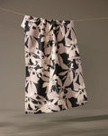 The Tawny tea towel by Geometry, featuring a beige and black abstract floral design, hangs over a thin rope against a neutral background.