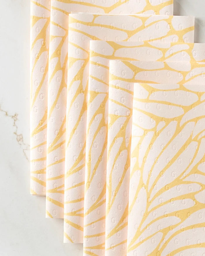 Five pale pink "Tenderhearted" reusable paper towels by GEOMETRY, featuring a gold abstract wing pattern, are arranged in an overlapping fan display on a white marble surface.