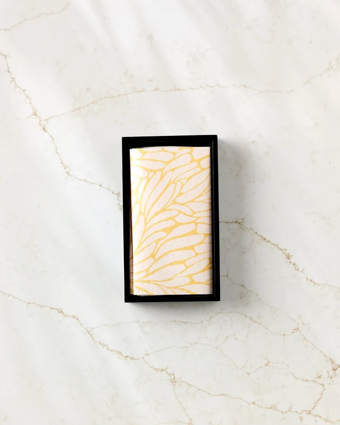 The GEOMETRY Tenderhearted rectangular soap, featuring a gold feather-like pattern, is displayed in a black box on white marble with light brown veining beside folded eco-friendly kitchen towels.