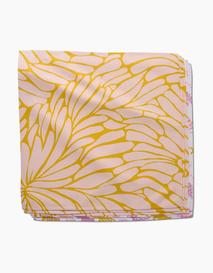 The GEOMETRY Tenderhearted Dinner Napkin is made from Geosuede fabric, showcasing a light pink base with a bold, abstract yellow petal-like pattern.