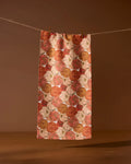 The Geometry Tendril towel, featuring an ultra-absorbent design with orange, brown, and beige pumpkin patterns, hangs on a string against a plain brown background, held by two wooden clothespins.